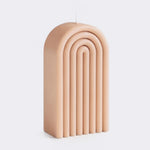 A candle with a ribbed, arch-shaped design in a warm peach-beige color, photographed on a clean light gray background.