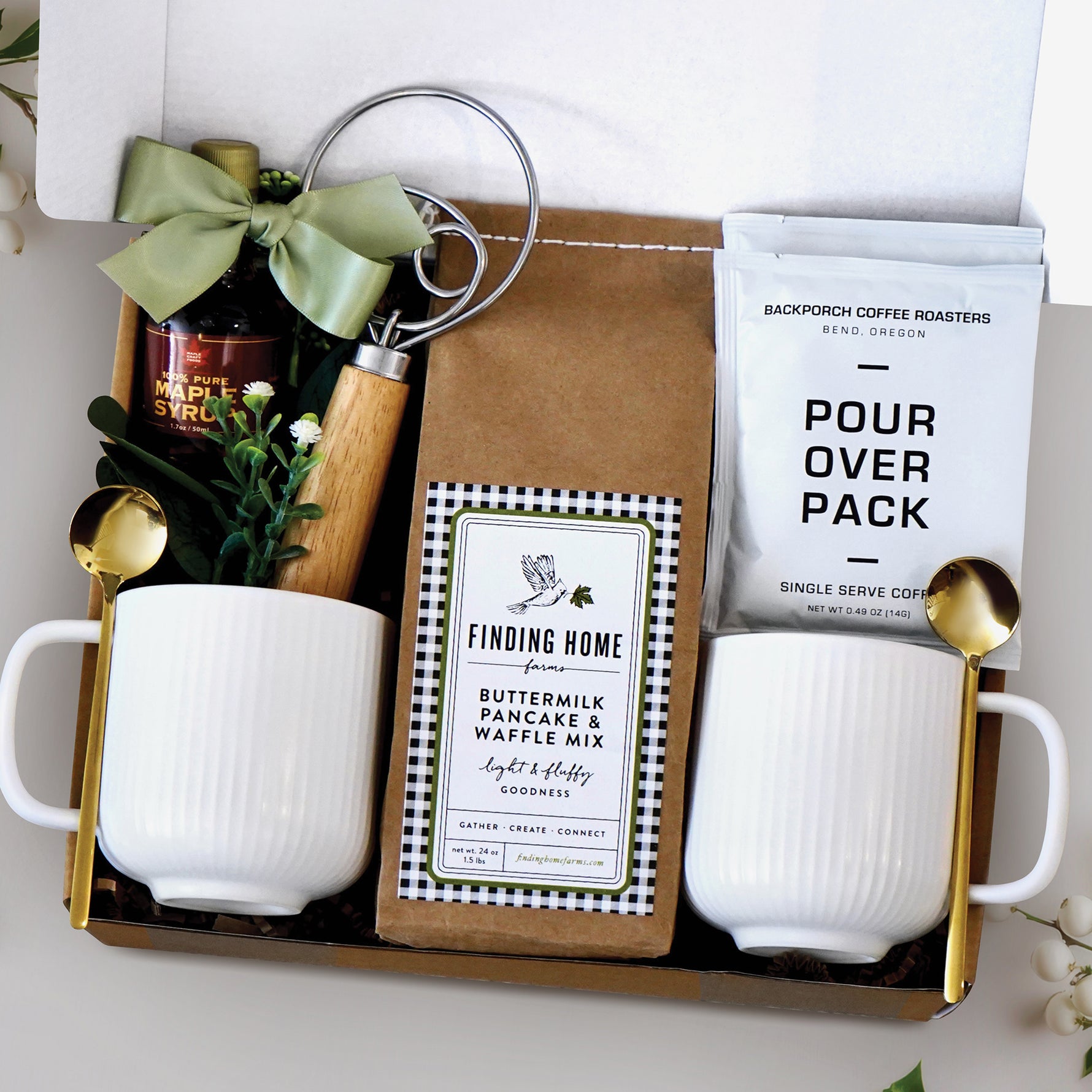 Breakfast for Two Gift Box for Couples includes 2 ceramic white ribbed mugs, 2 gold spoons, 1 dough whisk, 1 1.7oz maple syrup, 2 single serve coffee packs, and one 24oz pancake and waffle mix