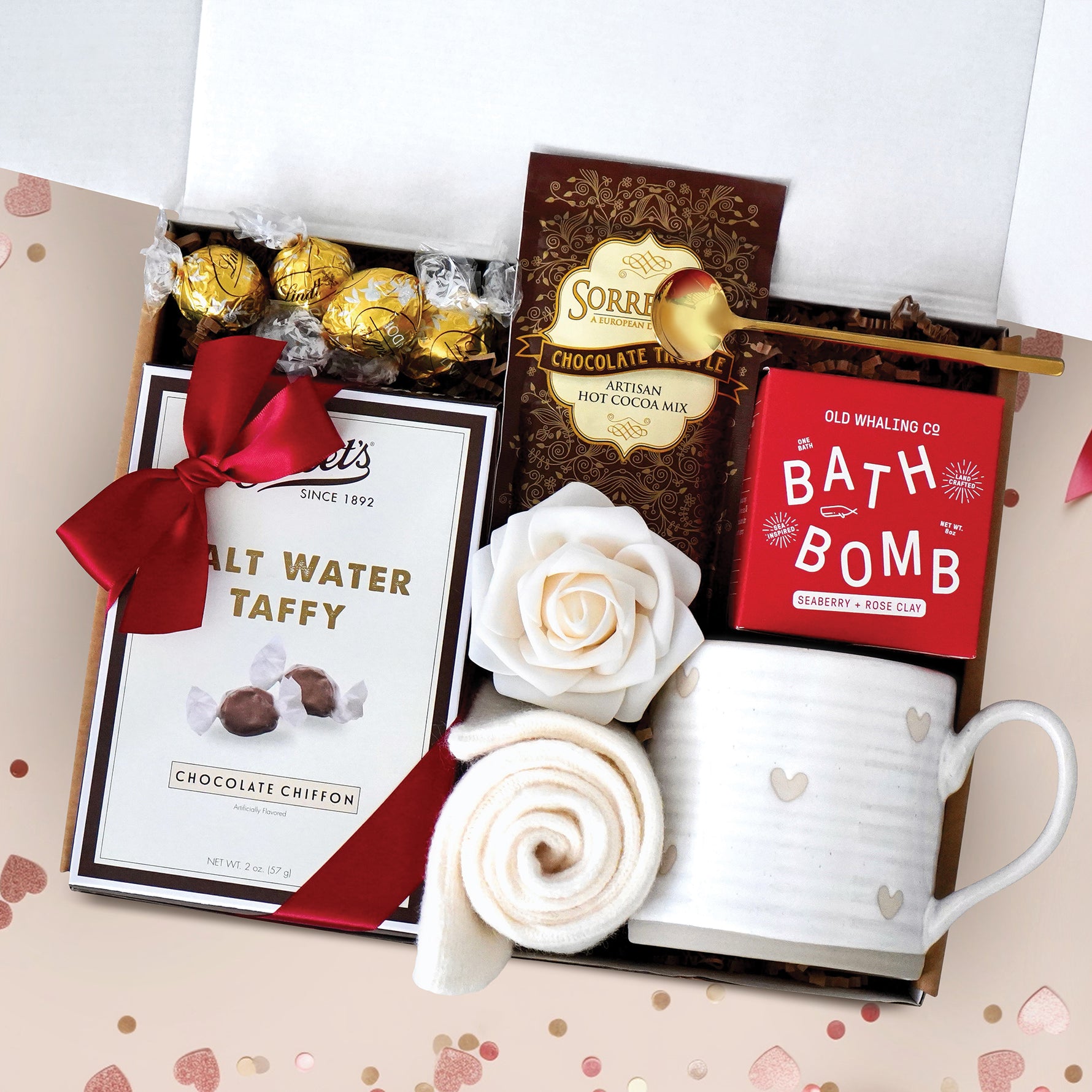 Chocolate Heart Gift Box comes with a rustic heart ceramic mug, gold demitasse spoon, Seaberry and Rose Bath Bomb, cream knit socks, chocolate salt water taffy, chocolate truffles, chocolate truffle hot cocoa mix, and a faux rose head