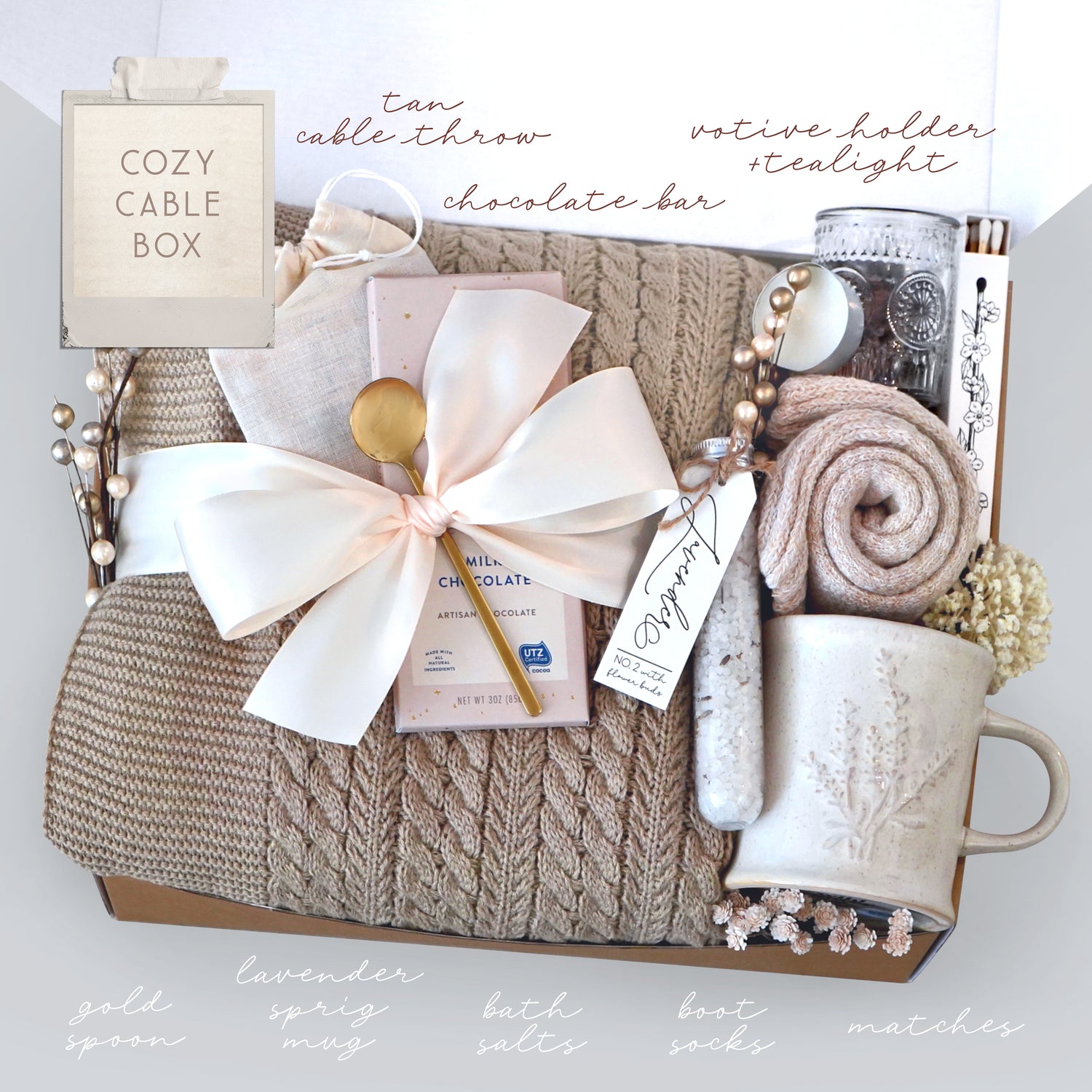 Cozy cable box with items including a mug, chocolate bar, and bath salts on a white background.