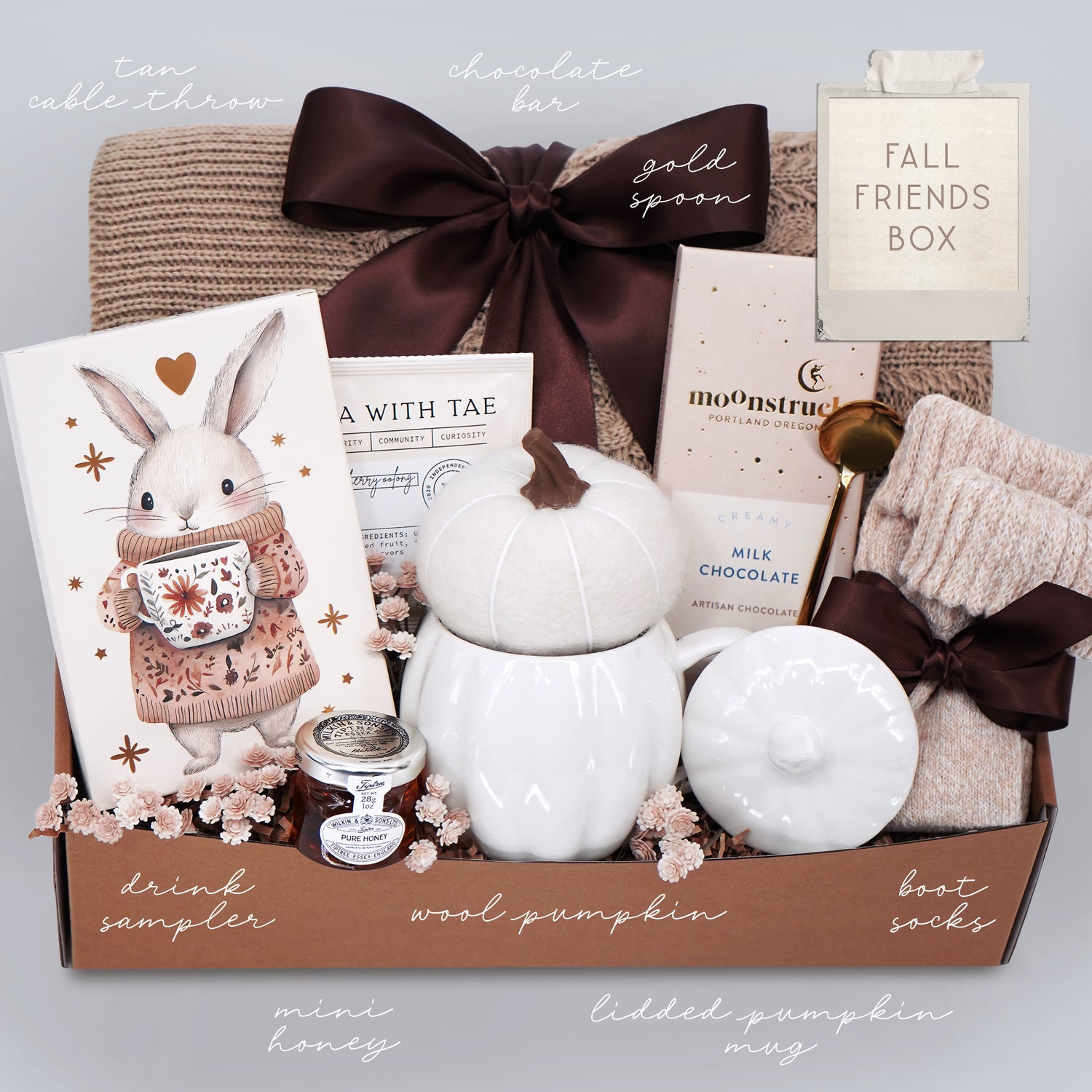 Gift box with various items including a pumpkin mug, boot socks, and a drink sampler on a light gray background.