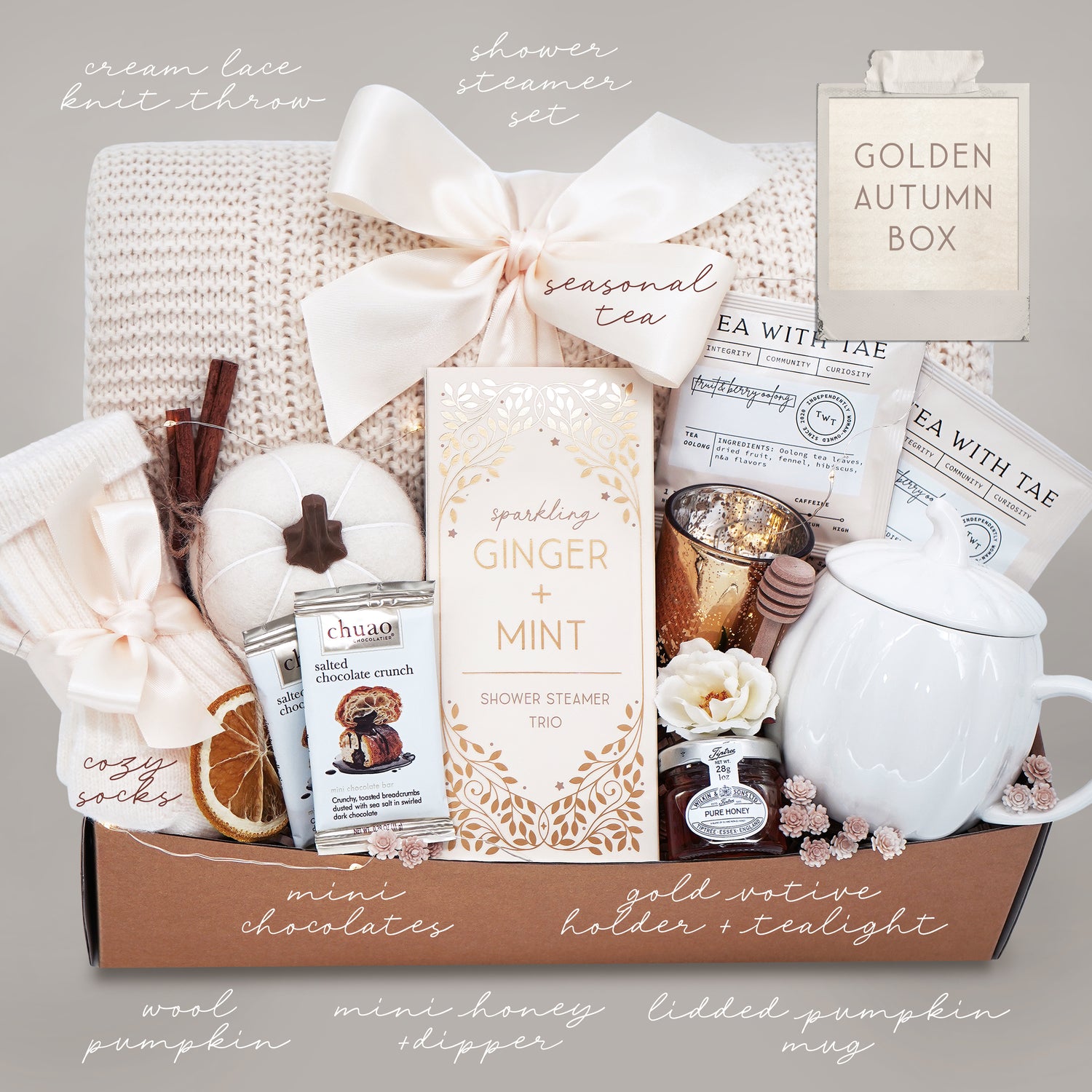 Gift box with various items including a tea set, pumpkin, and candles on a neutral background.