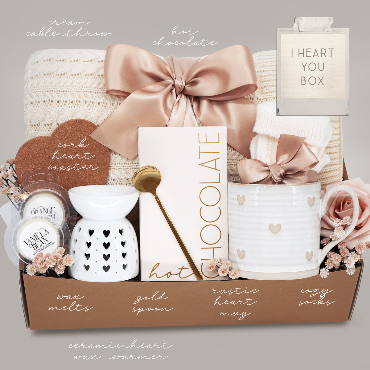 Gift set with a heart mug, wax warmer, cable knit blanket, hot chocolate, wax melts, and heart coaster on a grey background