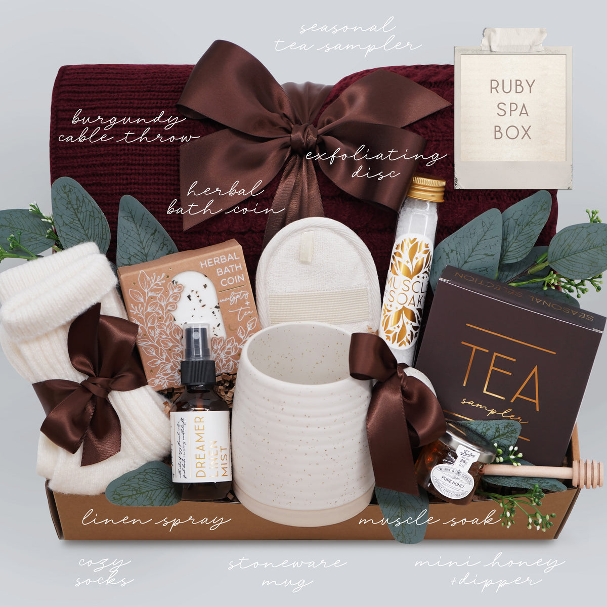 Wildflower Pop Ruby Spa Box with Burgundy blanket, bath salts, bath bomb, linen mist, cream socks, tea sampler, and mini honey and dipper. On light grey background