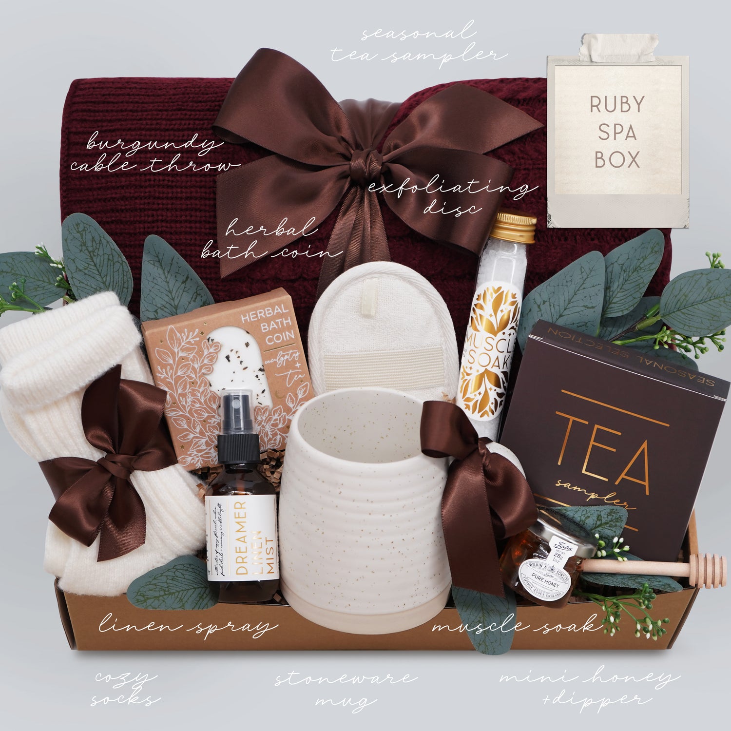 Wildflower Pop Ruby Spa Box with Burgundy blanket, bath salts, bath bomb, linen mist, cream socks, tea sampler, and mini honey and dipper. On light grey background