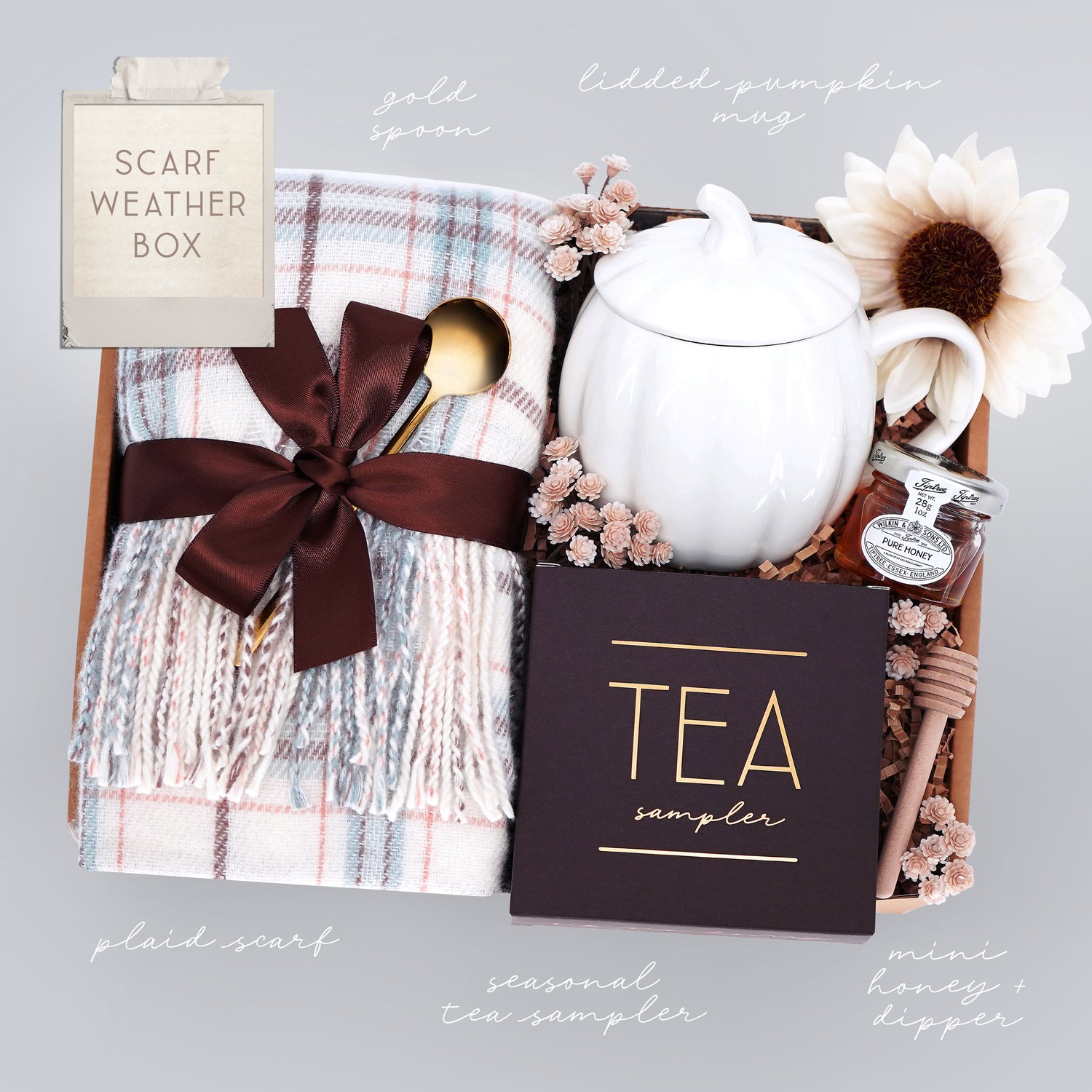 Gift set with plaid scarf, tea sampler, and honey dipper on a gray background