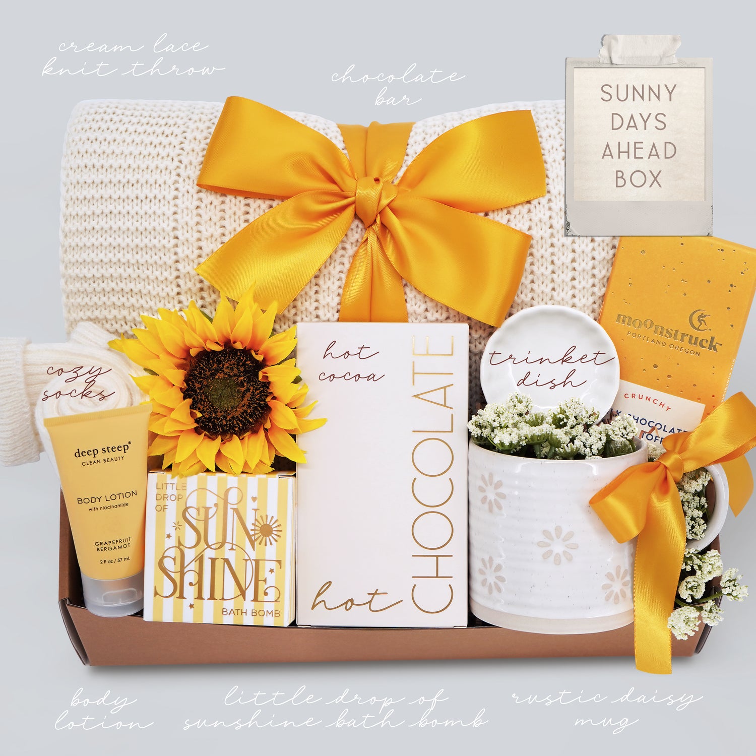 Gift box with various items including a sunflower, chocolate bar, and other decorative elements on a light gray background.
