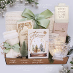 Gifting set with cozy socks, mini tree, drink sampler, glass mug, and sweet snow globe box on a light background.