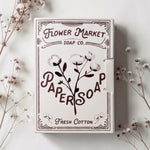 Flower Market Soap Co. Paper Soap in Fresh Cotton scent. Cream-colored packaging with dark brown typography and cotton illustrations, styled on a light surface with dried floral stems.