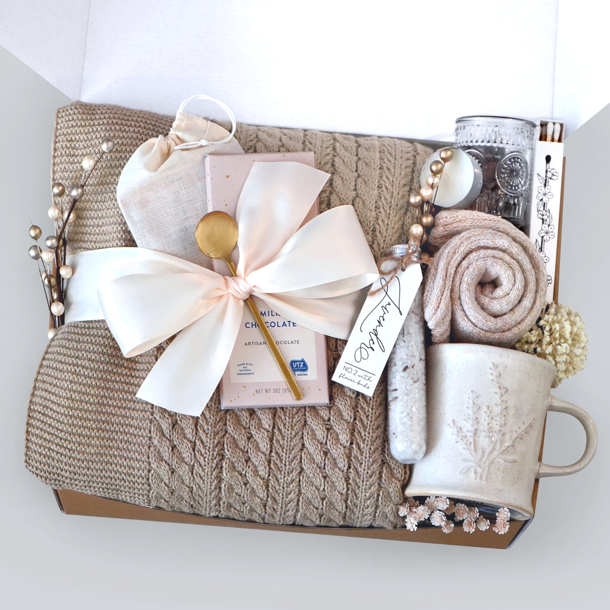 Gift basket with cable knit blanket, a mug, and decorative elements on a white background
