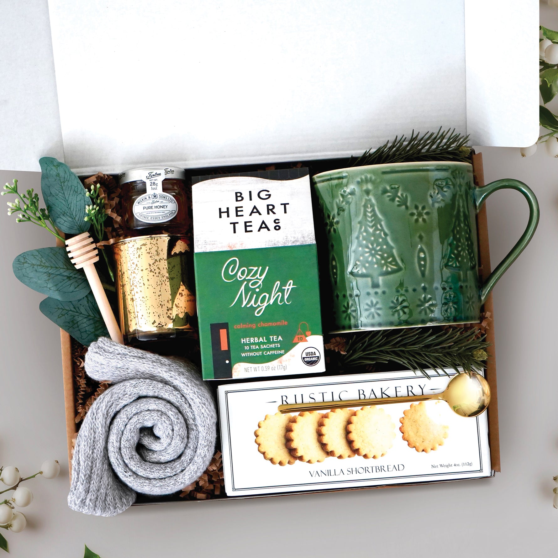 Cozy Night Tree Mug Box comes with a nordic tree ceramic mug, rustic bakery vanilla shortbread cookies, gold demitasse spoon, mini honey and dipper, cozy night 10 count tea bags, cozy boot socks, and gold votive and tea light