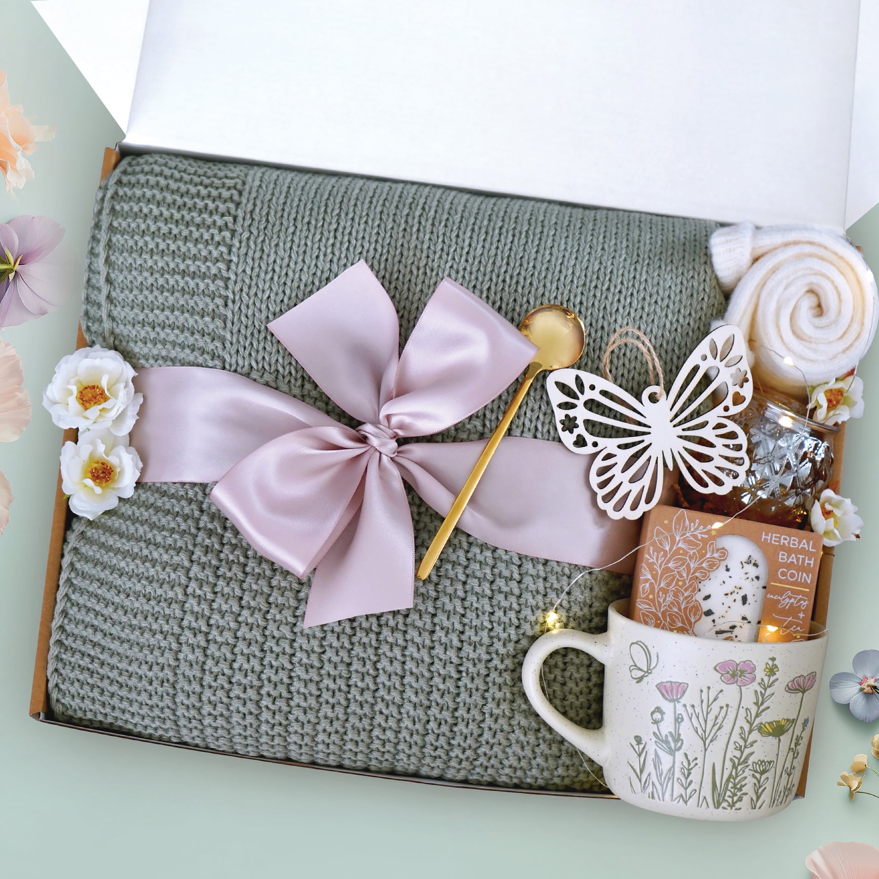 Our fairy garden blanket box comes with a sage green lace knit blanket, wildflower ceramic mug, votive and tea light, a string of fairy lights, cozy knit socks, a Wildflower Pop Eucalyptus and tea bath coin, wooden nordic butterfly ornament, and a gold demitasse spoon. The perfect gift for a beloved teacher helping your child grow.