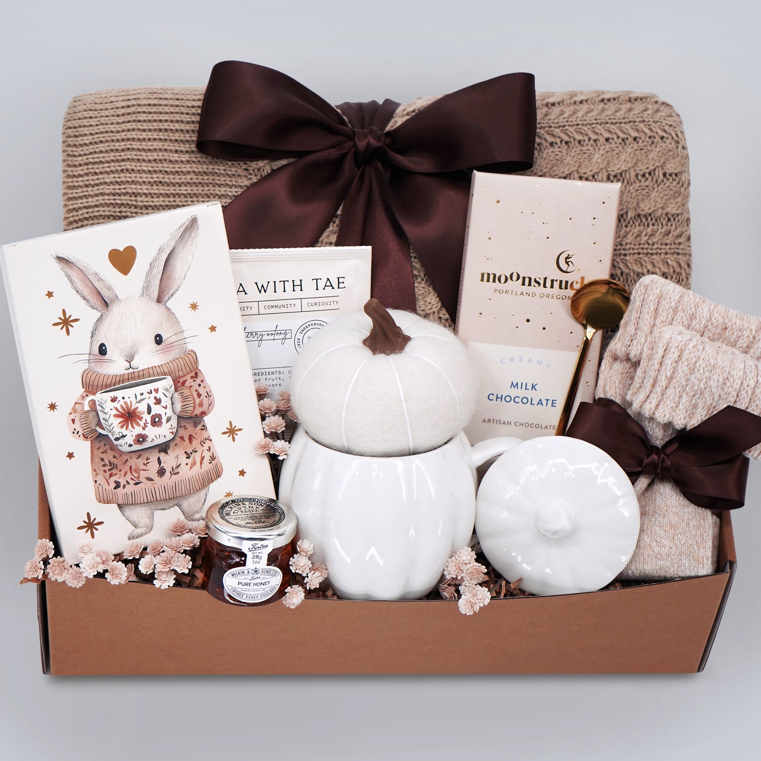 Gift basket with a blanket, drink sampler, and decorative items on a light gray background