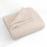A folded cream-colored cable-knit blanket with a ribbed border, displayed on a clean white background.