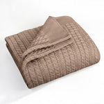 A folded tan-colored cable-knit blanket with a ribbed border, displayed on a clean white background.