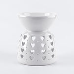 A white ceramic wax warmer/diffuser with a heart-shaped cutout pattern, set against a light gray background.