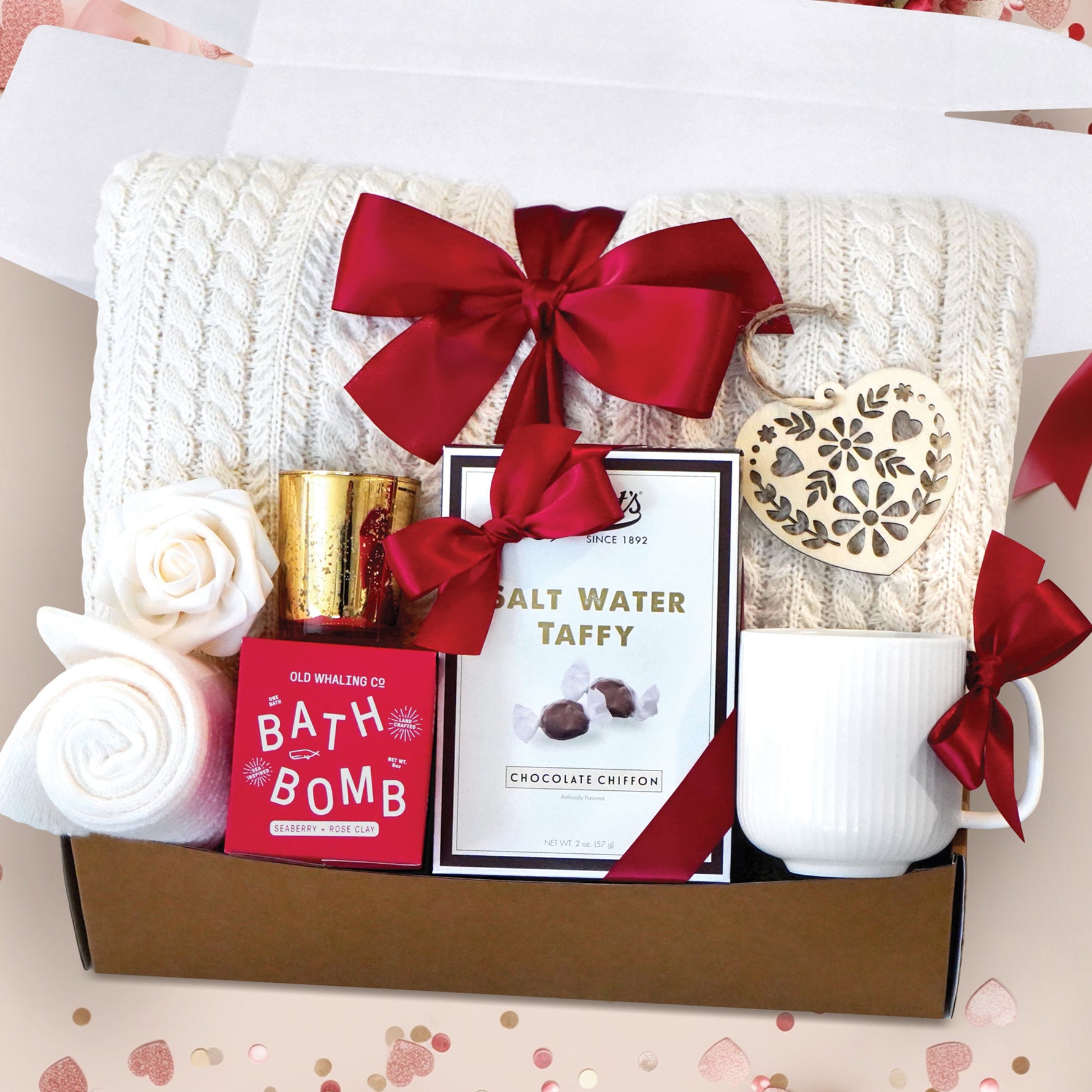 Hello Cupid Gift Box comes with a cream cable knit blanket tied with a red ribbon, cream knit socks, gold votive and tea light, Seaberry and Rose bath bomb, Chocolate Chiffon salt water taffy, nordic heart wood ornament, faux rose head, and cream ribbed mug