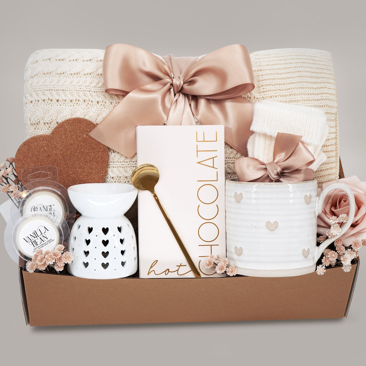 Gift set with a heart mug, wax warmer, cable knit blanket, hot chocolate, wax melts, and heart coaster on a grey background