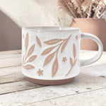 Ceramic mug with leaves and flower details on wood background