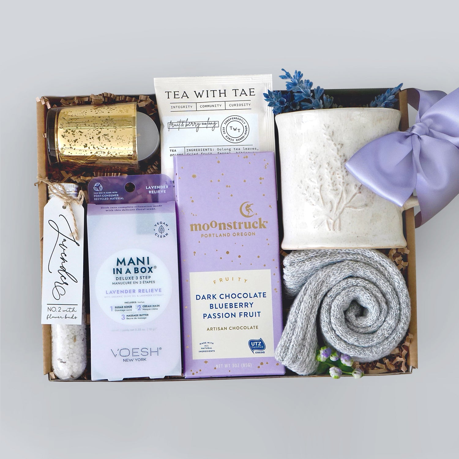 Lavender Gift box with various spa items including a candle, tea, and chocolate on a light gray background