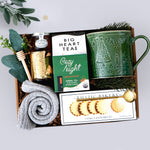 Wildflower Pop Gift set with a green mug, tea packaging, and cookies in a decorative box, grey cozy socks, gold votive, and mini honey and dipper on grey background