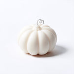 A small white pumpkin-shaped candle set against a clean white background.