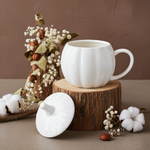 White ceramic pumpkin mug and lid on a wooden block with decorative elements on a brown background