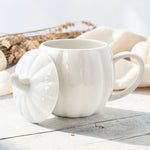 White ceramic pumpkin shaped mug with a matching stem lid on a wooden surface