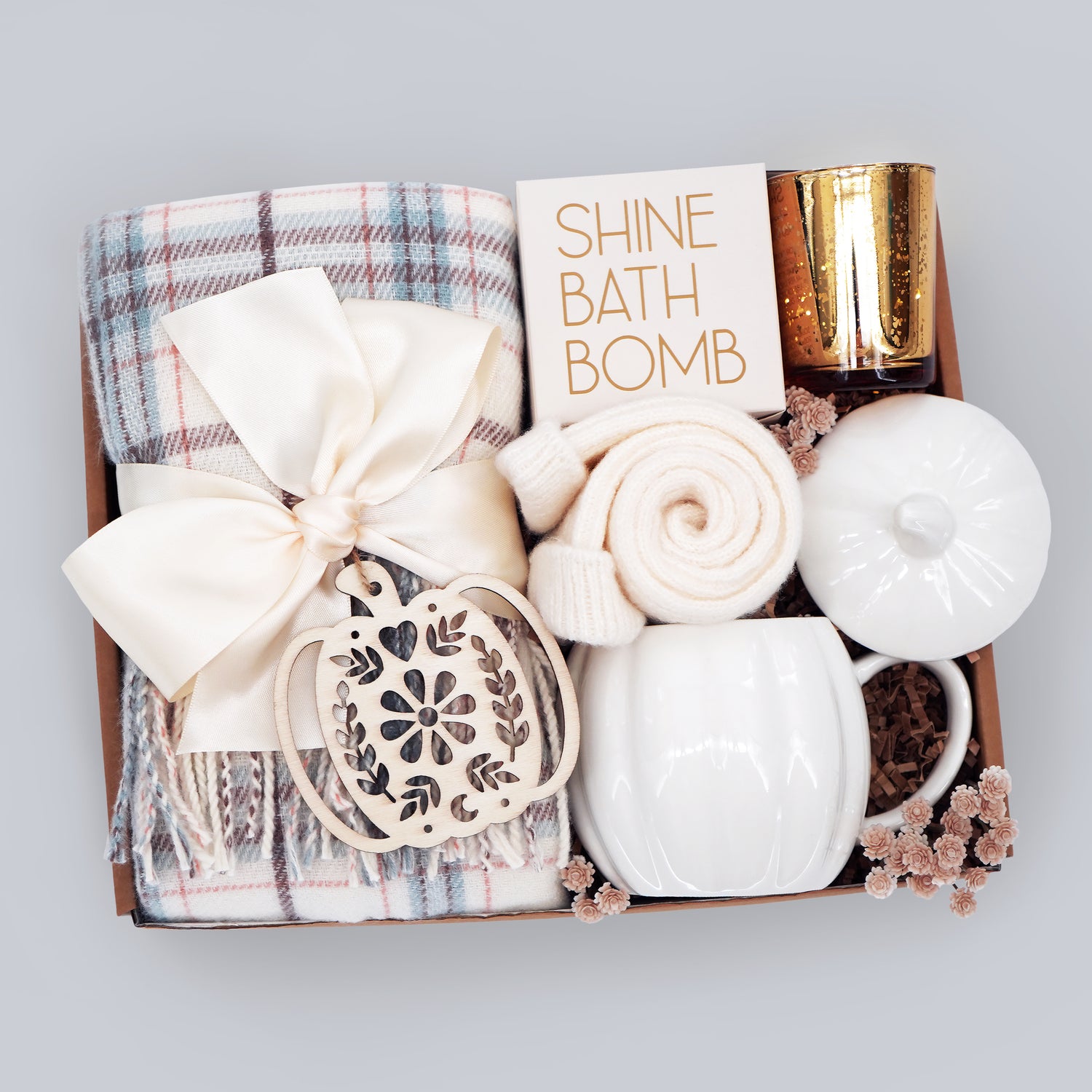 Gift box with a plaid scarf, bath bomb, candle, and other items on a light gray background