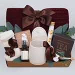 Wildflower Pop Ruby Spa Box with Burgundy blanket, bath salts, bath bomb, linen mist, cream socks, tea sampler, and mini honey and dipper. On light grey background