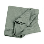 A folded dusty sage-colored lace knit blanket with textured patterns, shown on a solid white background.