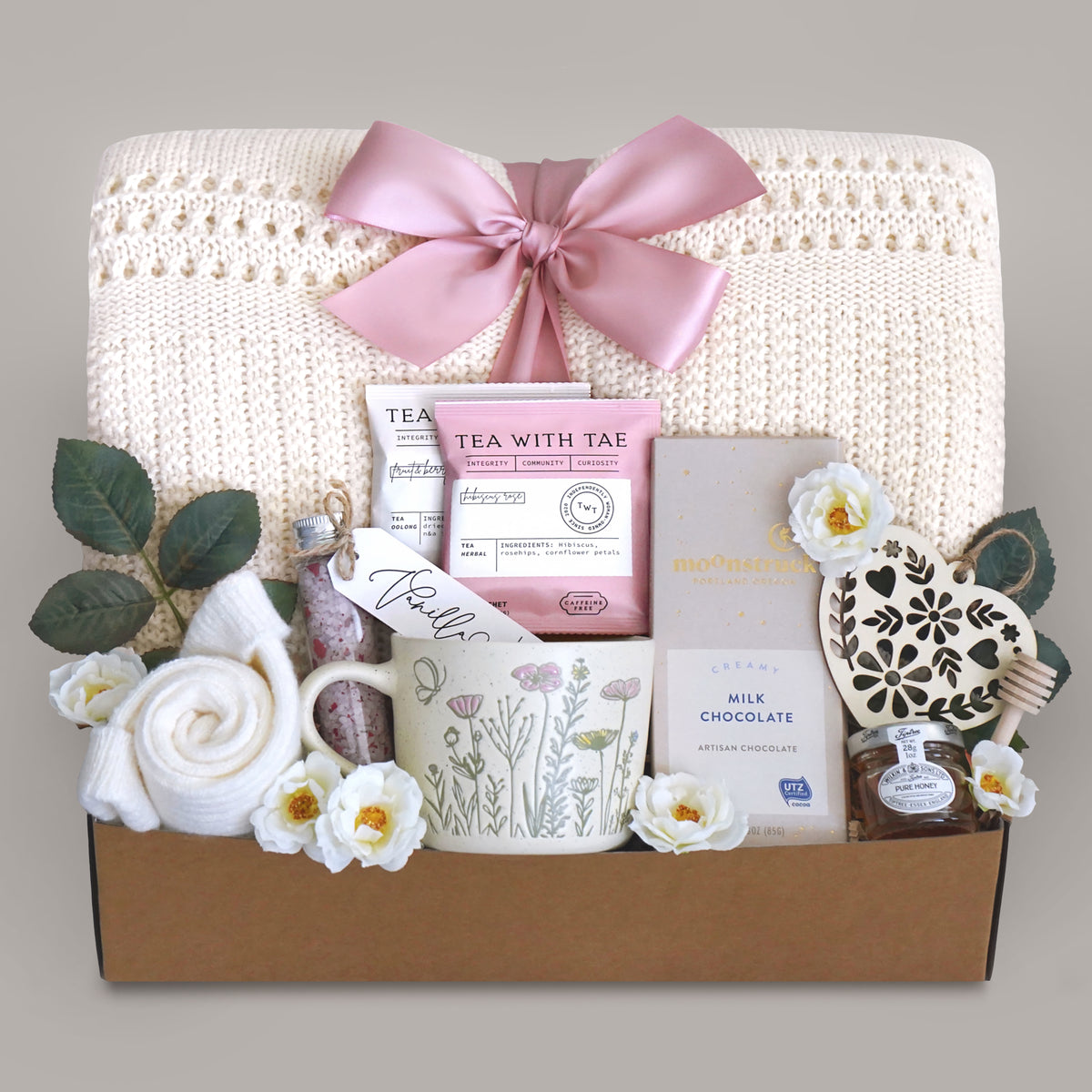 Sending Flowers Gift blanket box with tea, chocolate, and decorative items on a gray background
