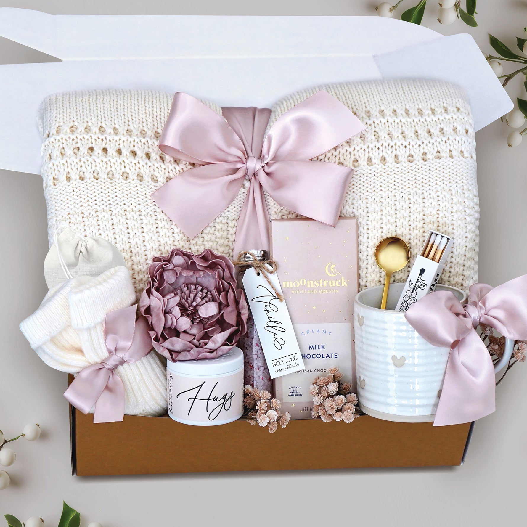 Sending Hugs Gift Box with a cream lace knit blanket, heart ceramic mug, matches, bath salt tube, faux peony head, cream knit socks, moonstruck milk chocolate bar. Finished with blush ribbon and packaged in a branded Wildflower Pop Gift Box