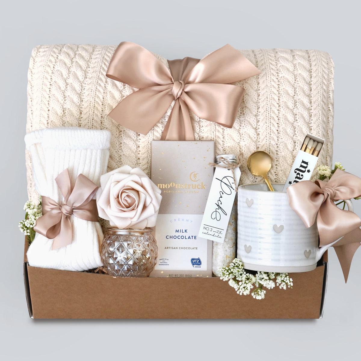 Gift box with a blanket, chocolate, and decorative items on a light gray background