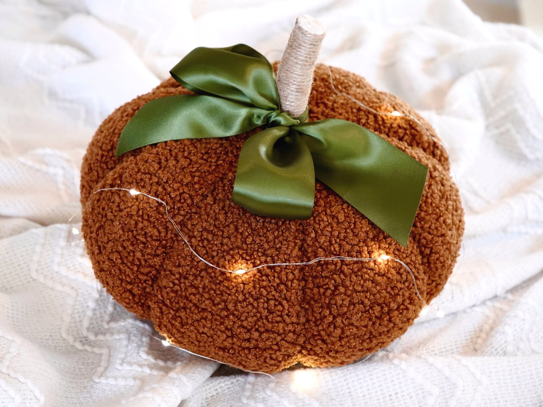 Sherpa Pumpkin Pillow in Orange tied with a moss green bow, measures around 10"