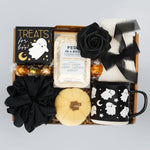 Gift box with Halloween-themed items including a mug, black roses, and candy on a light gray background.
