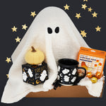 Halloween-themed gift set with ghost pillow, pumpkin, Wildflower Pop Ghost mug, and candy on a dark background.