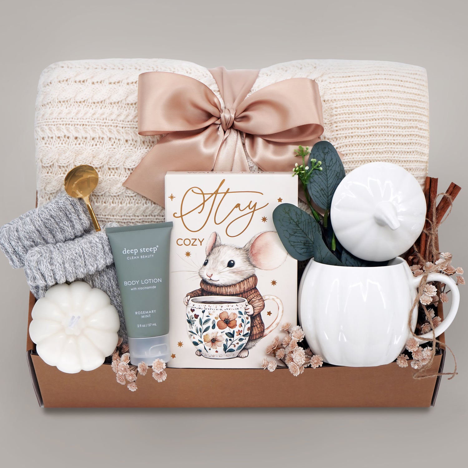 Gift basket with cozy items including a mug, candle, and body lotion on a neutral background