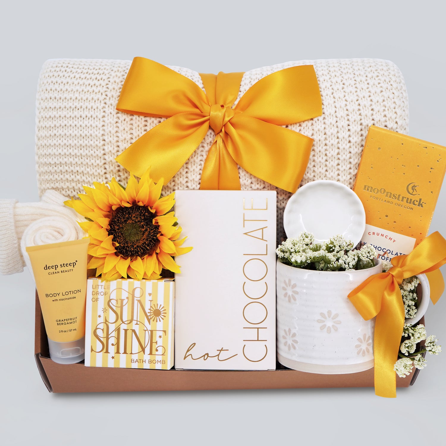 Gift set with sunflower, chocolate bar, and other items on a light gray background