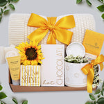 Wildflower Pop Sunny Days Ahead blanket gift box with a cream lace knit blanket, Wildflower Pop daisy ceramic mug, scallop trinket dish, moonstruck milk chocolate and toffee bar, little drop of sunshine bath bomb, faux sunflower, deep steep lotion, and cream knit socks
