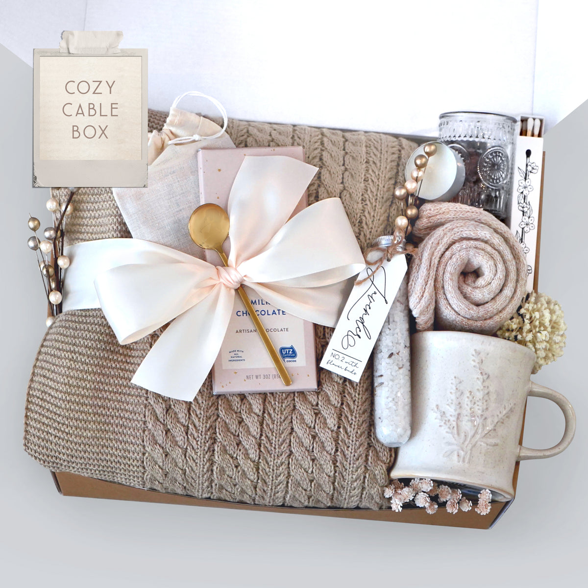 Gift basket with cable knit blanket, a mug, and decorative elements on a white background