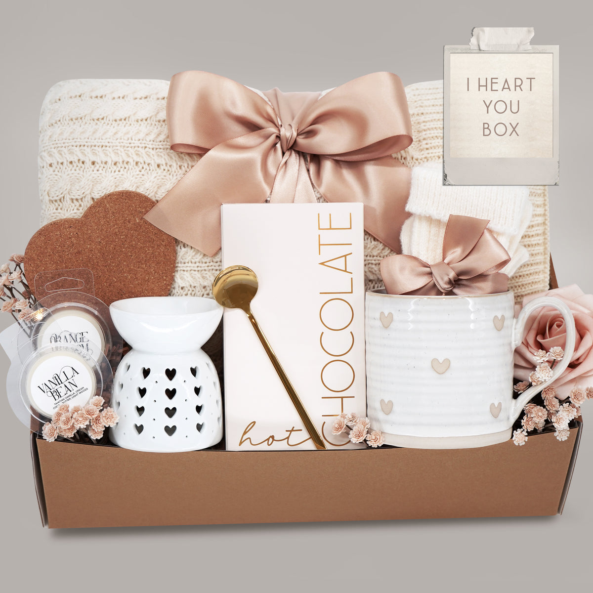 Gift set with a heart mug, wax warmer, cable knit blanket, hot chocolate, wax melts, and heart coaster on a grey background