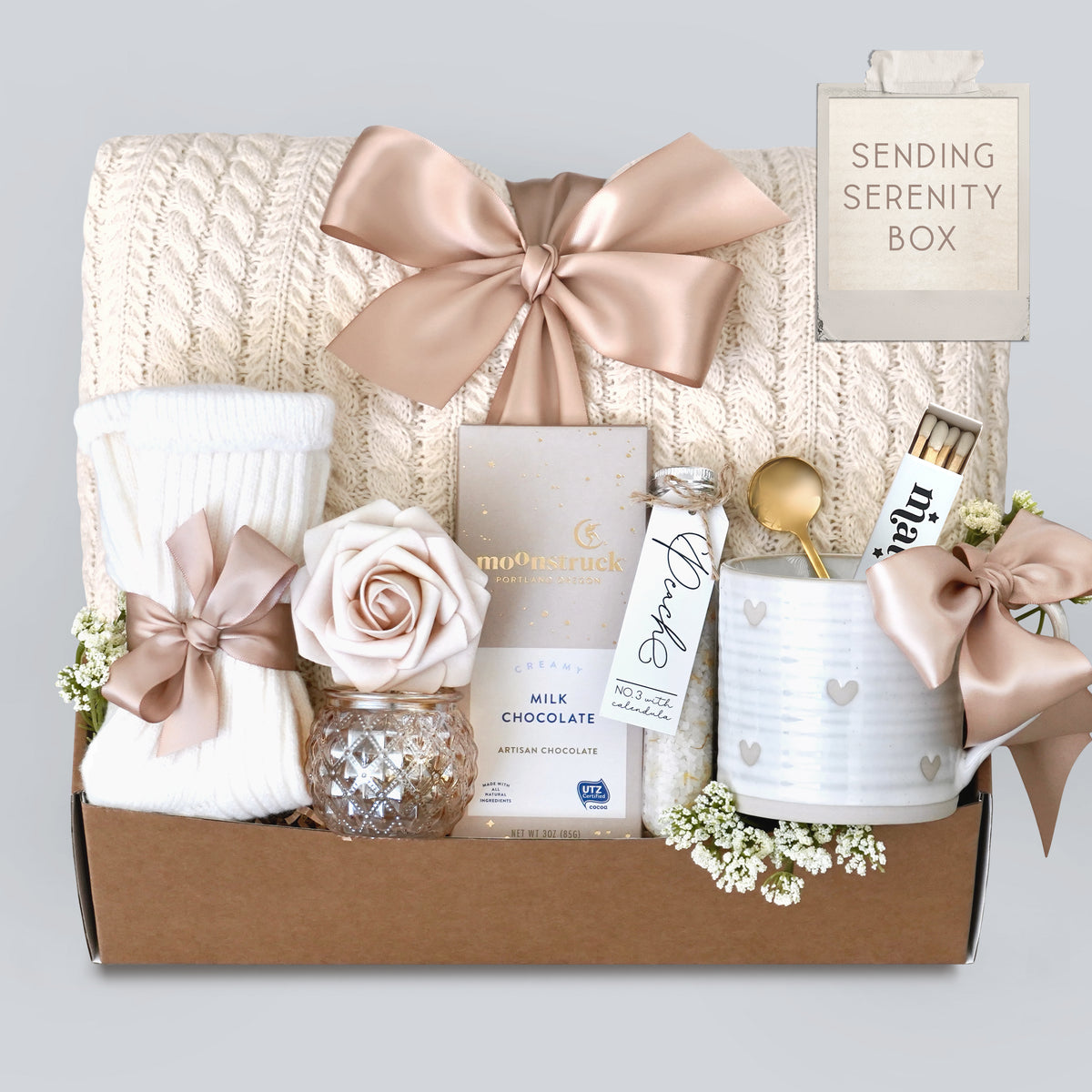 Gift box with a blanket, chocolate, and decorative items on a light gray background