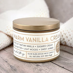 Candle labeled 'Warm Vanilla Cream' on a wooden surface with soft background