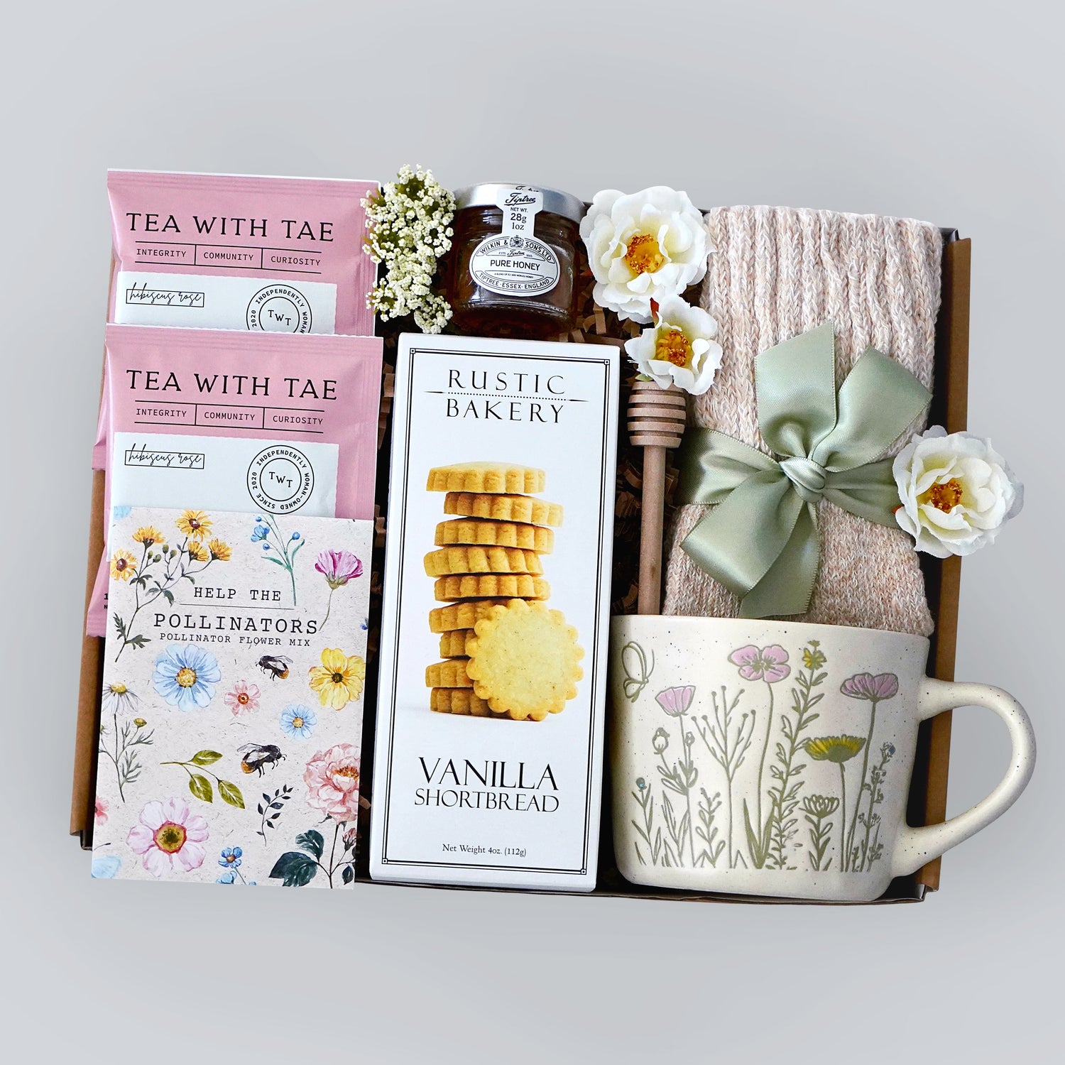 Gift set with tea, cookies, mug, and honey with dipper on a gray background