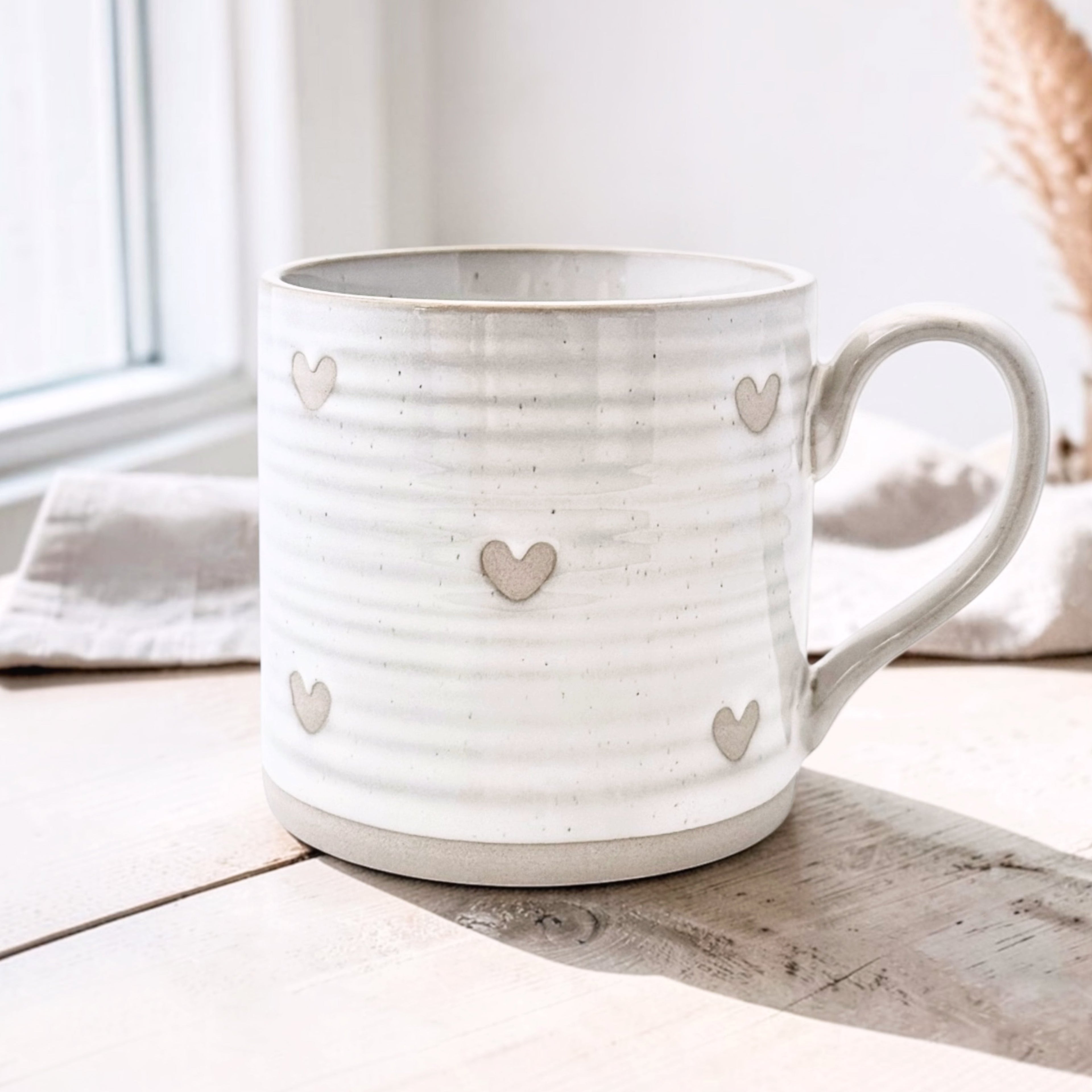 Wildflower Pop Exclusive Designed by us White mug with heart patterns on a textured beige surface