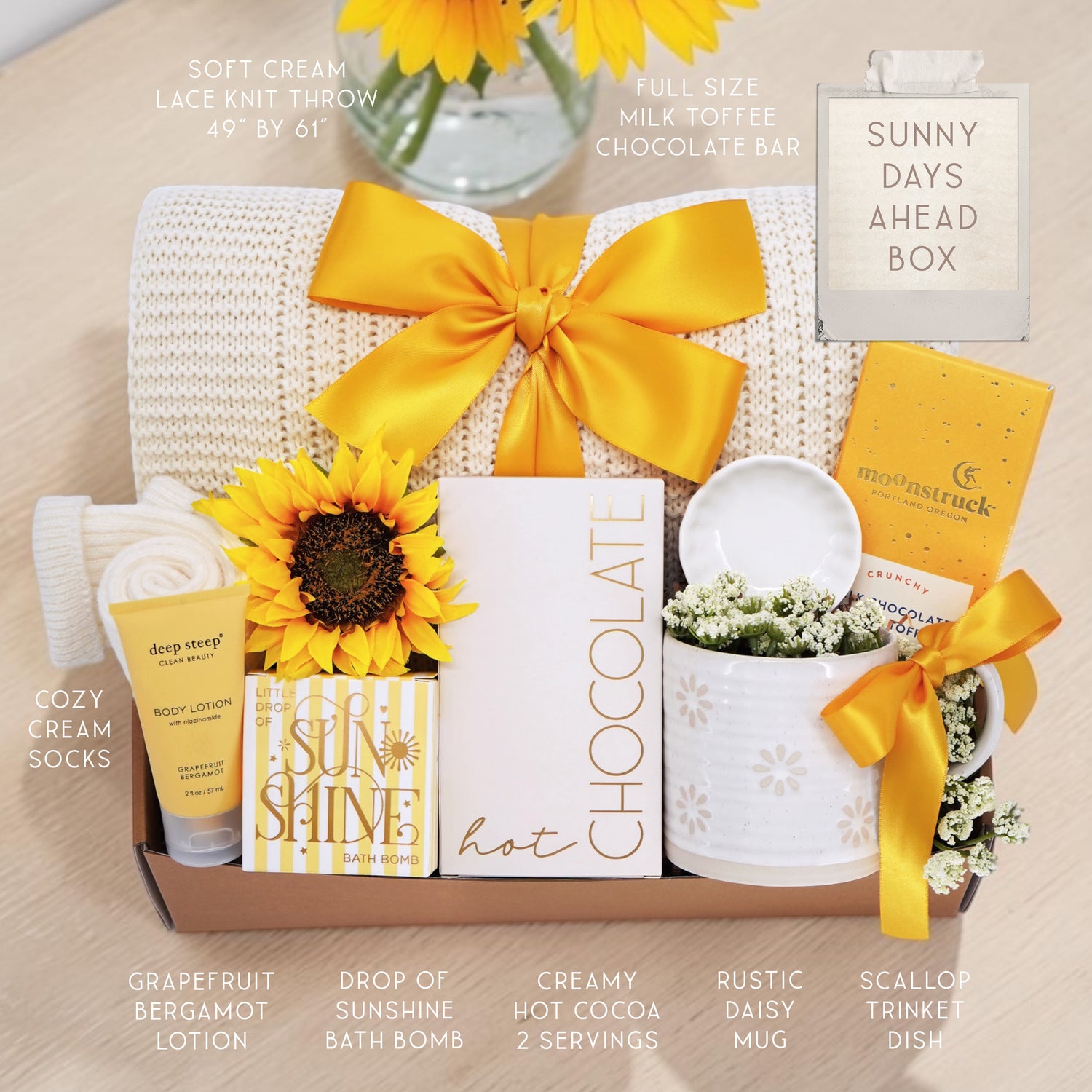 Wildflower Pop Sunny Days Ahead blanket gift box with a cream lace knit blanket, Wildflower Pop daisy ceramic mug, scallop trinket dish, moonstruck milk chocolate and toffee bar, little drop of sunshine bath bomb, faux sunflower, deep steep lotion, and cream knit socks