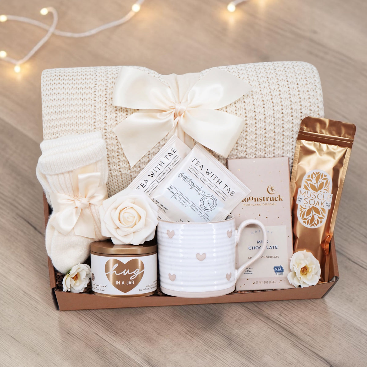 Wildflower Pop Sending a Hug Blanket gift box, with cream lace knit blanket, tea sampler, cream knit socks, hug in a jar soy wax candle, Wildflower Pop Heart ceramic mug, Moonstruck Milk Chocolate bar, and muscle soak