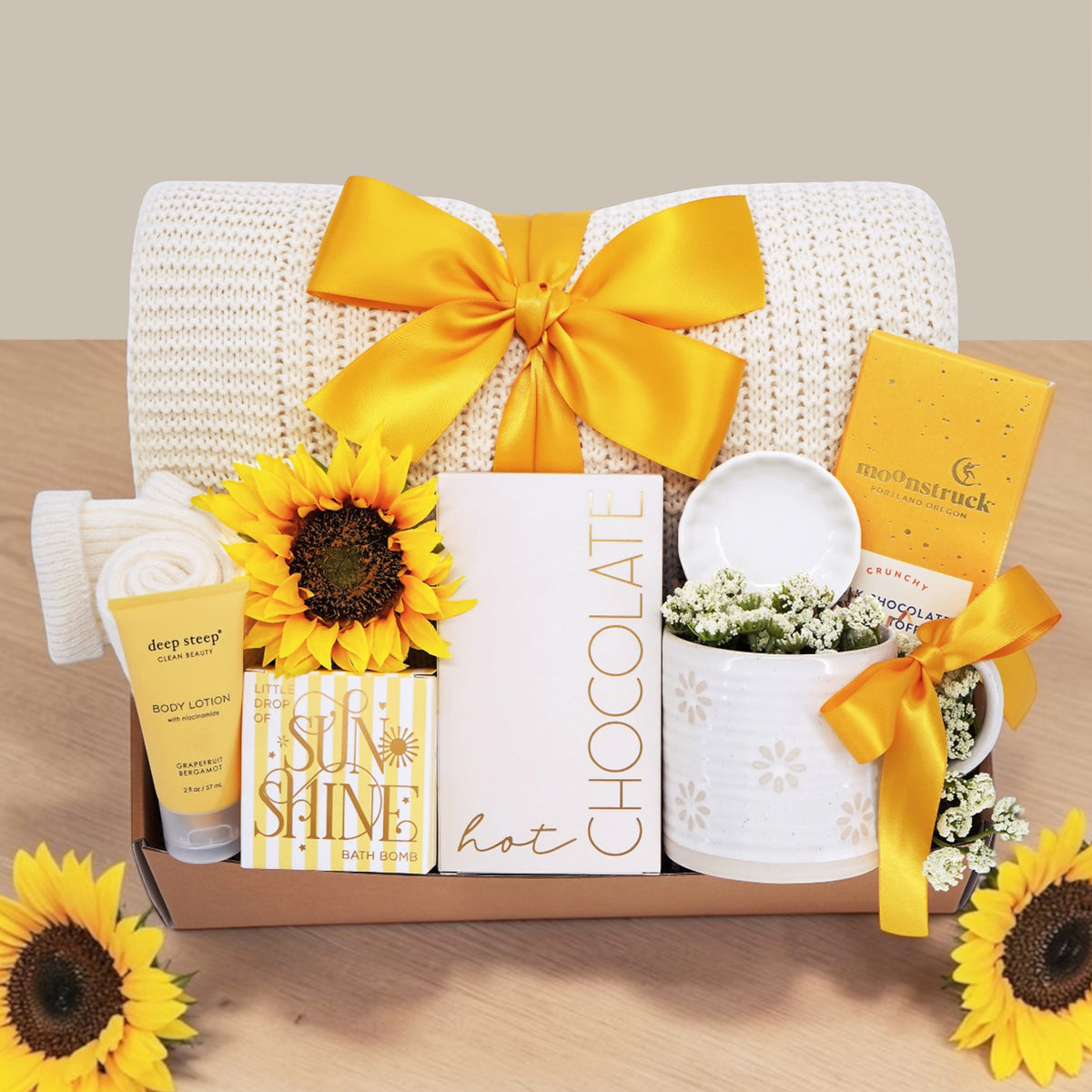 Wildflower Pop Sunny Days Ahead blanket gift box with a cream lace knit blanket, Wildflower Pop daisy ceramic mug, scallop trinket dish, moonstruck milk chocolate and toffee bar, little drop of sunshine bath bomb, faux sunflower, deep steep lotion, and cream knit socks