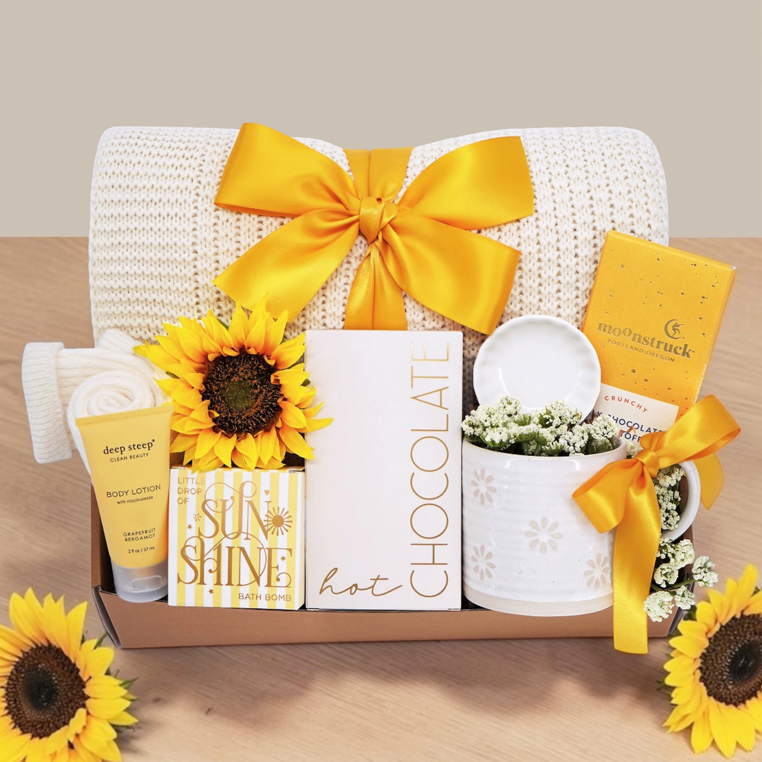 Wildflower Pop Sunny Days Ahead blanket gift box with a cream lace knit blanket, Wildflower Pop daisy ceramic mug, scallop trinket dish, moonstruck milk chocolate and toffee bar, little drop of sunshine bath bomb, faux sunflower, deep steep lotion, and cream knit socks